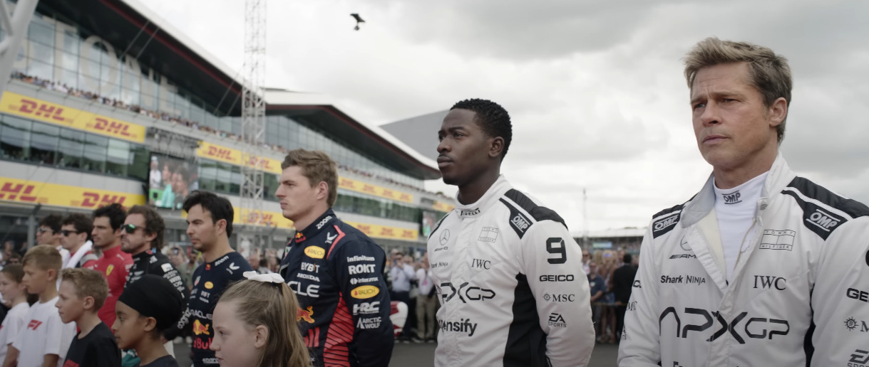 Brad Pitt and Joshua Pierce standing together, gearing up for the Formula 1 race